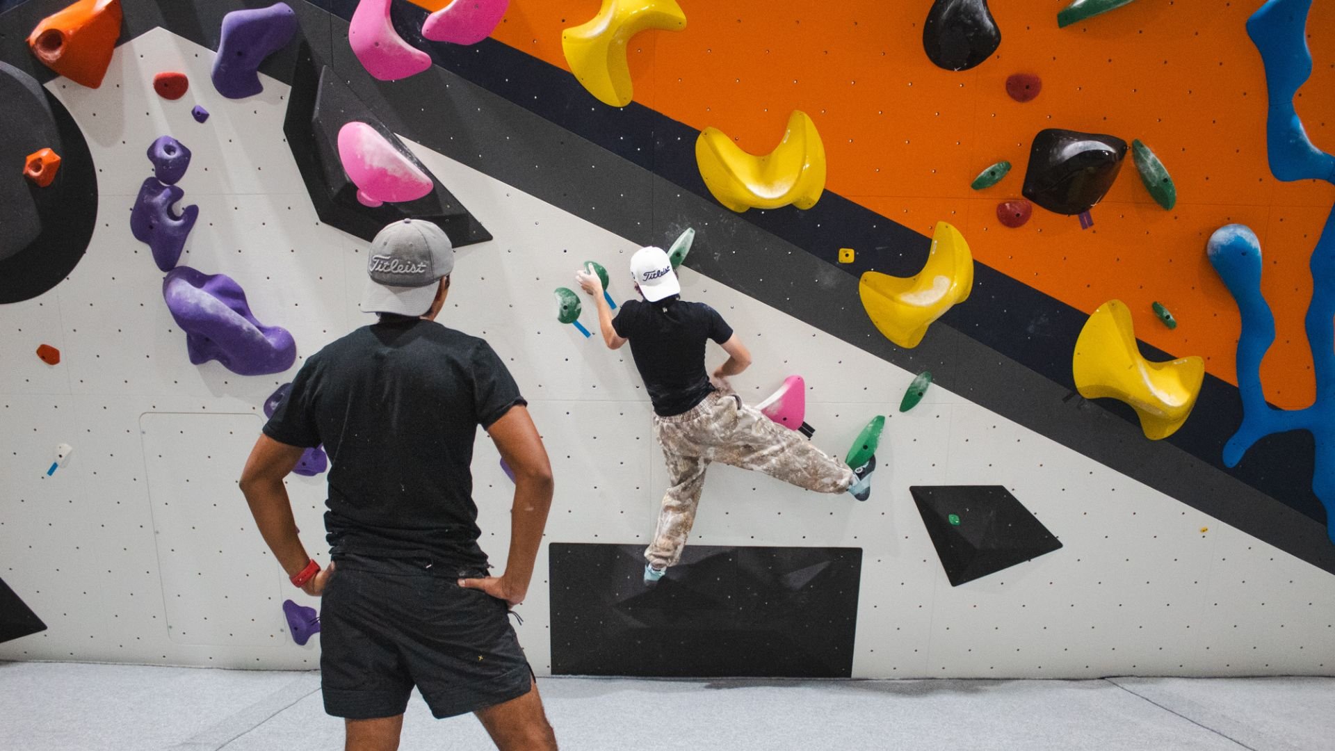 A climber sticks a toe hook at the Lubbock gym as another climber looks on