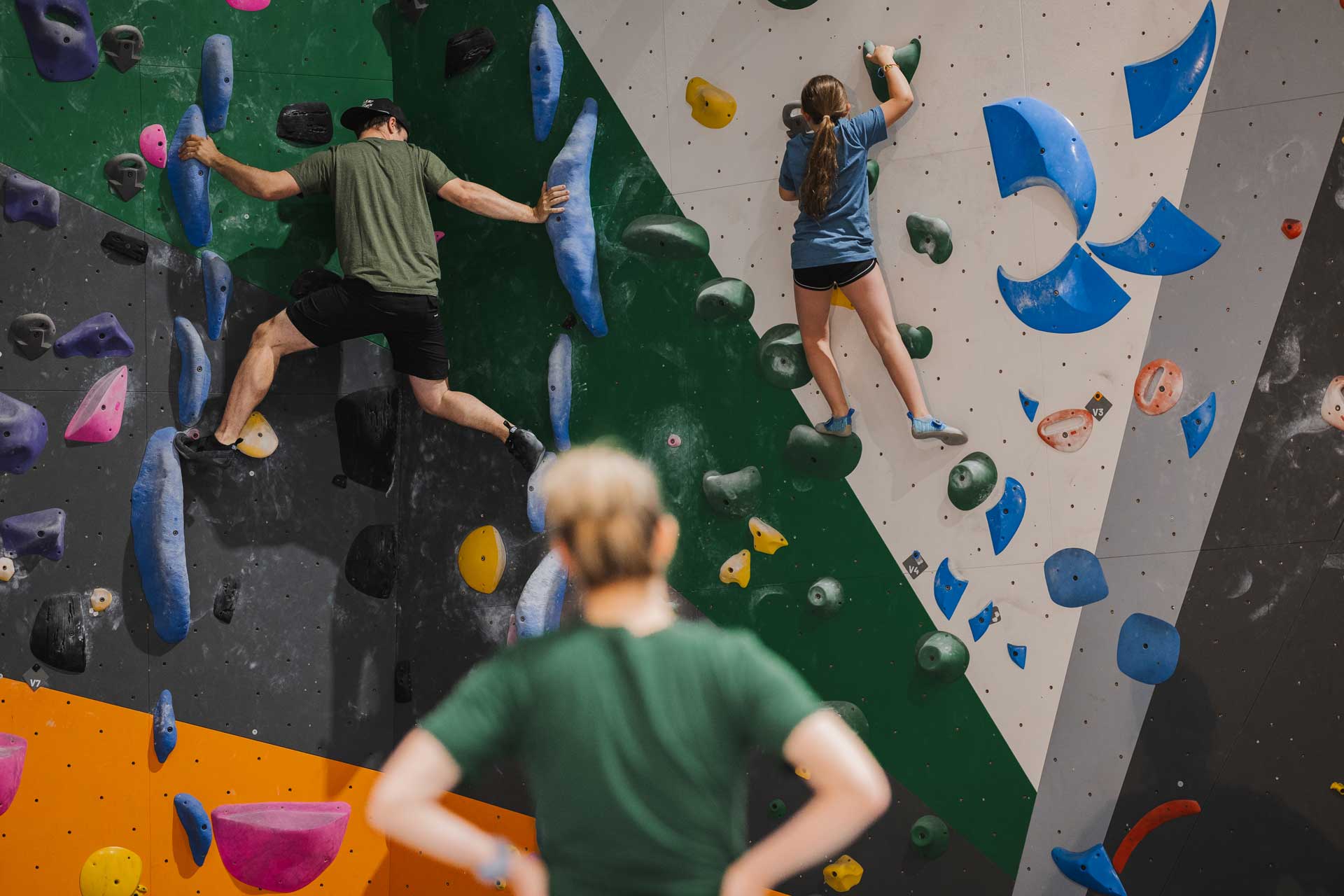 A gym climber watches two others bouldering