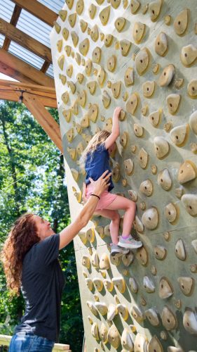 Lindsay Runne helping a young climber on a climbing wall